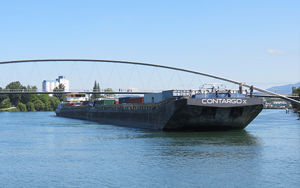 Un bateau chargé de conteneurs devant un pont sur le Rhin. 